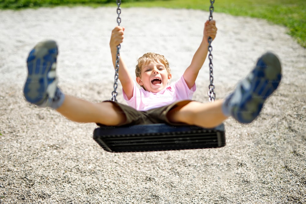 Funny kid boy having fun with chain swing on outdoor playground while being wet splashed with water. child swinging on summer day. Active leisure with kids. Happy crying boy with rain drops on face