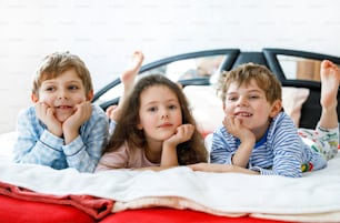 Three happy kids in pajamas celebrating pajama party. Preschool and school boys and girl having fun together. Children playing together in bed. Making pillow fight