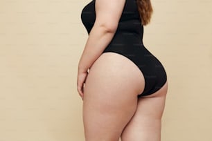 Plus-Size-Modell. Frau Hüften nah dran. Fetter Torso im schwarzen Body. Vollfigurige Frau posiert auf beigem Hintergrund. Body Positives Konzept.