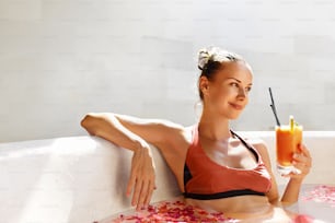 Detox Diet And Summer Relax. Beautiful Sexy Happy Smiling Woman Drinking Fresh Detox Juice Cocktail, Healthy Drink While Bathing, Relaxing In Outdoor Flower Bath In Luxury Day Spa Salon On Vacation