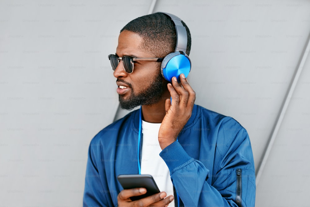 Ascolta musica. Uomo con le cuffie e il telefono in abiti di moda. Bel maschio nero che ascolta musica all'aperto. Alta risoluzione