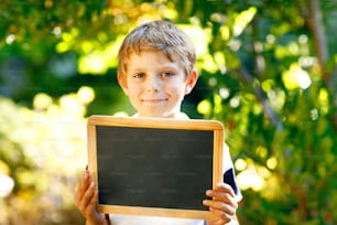 Happy little kid boy with chalk desk in hands. Healthy adorable child outdoors Empty desk for copyspace holding by beautiful schoolkid.