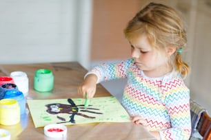 Little creative toddler girl painting with finger colors an owl bird. Active child having fun with drawing at home, in kindergaten or preschool. Games, education and distance learning for kids.