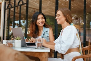 Mujeres trabajando en una computadora portátil en un café. Hermosas chicas étnicas con ropa casual discutiendo sobre negocios en la terraza. Estilo de vida nómada digital para un trabajo cómodo en la cafetería.