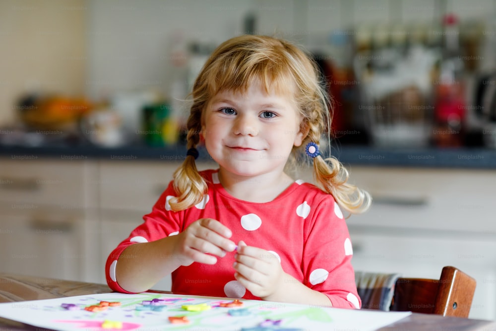 Little toddler girl playing with different colorful stickers and painting flowers. Concept of activity of children during pandemic corona virus quarantine. Child learning colors with parents at home.