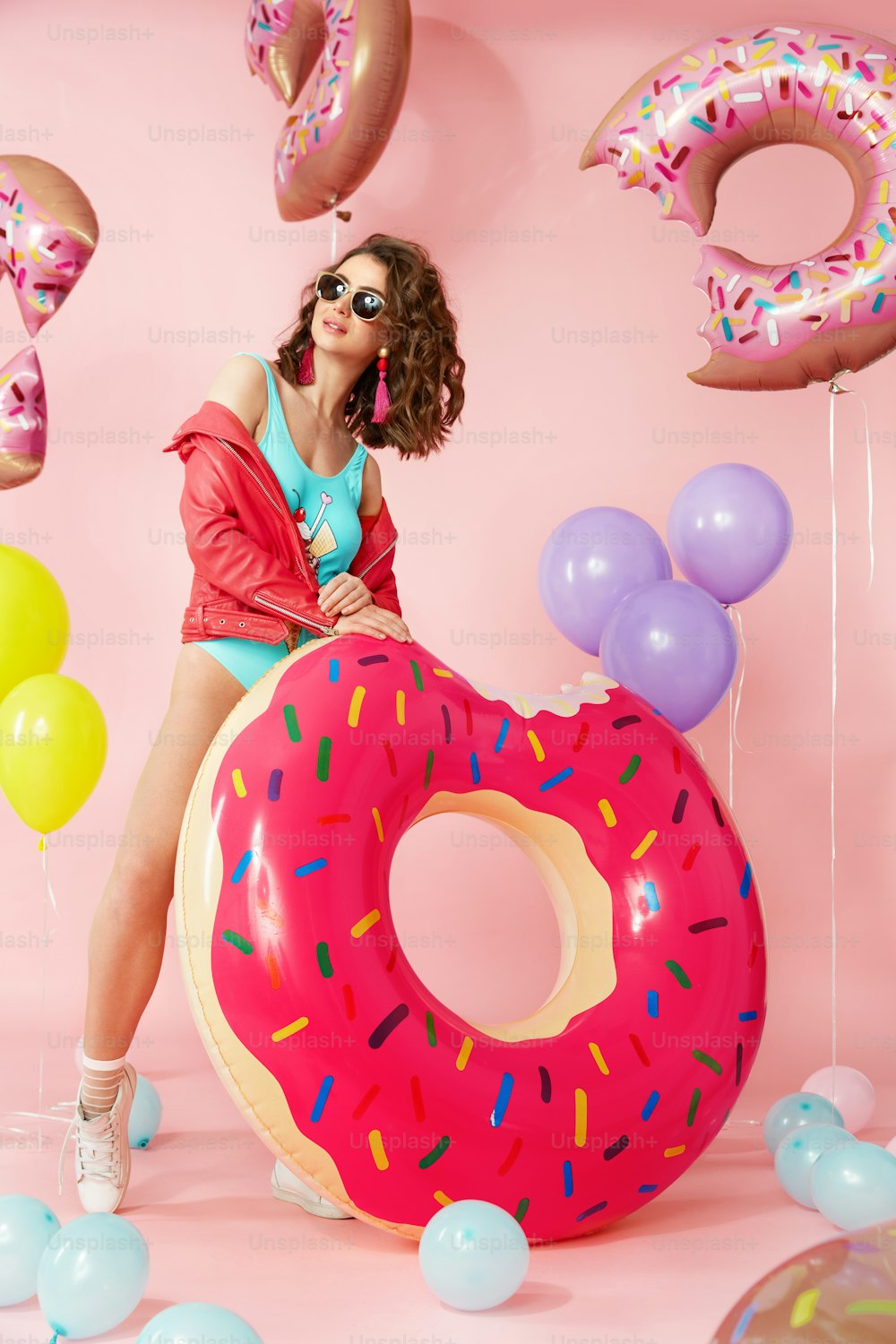 Moda de verano. Mujer en traje de baño con globos. Hermosa modelo femenina joven feliz con cuerpo en forma en trajes de baño coloridos de moda con flotadores de rosquilla inflables en Pink Bakcground. Alta resolución.