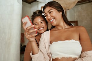 Mädchen, die Selfie machen. Freunde, die das Smartphone zum Fotografieren verwenden. Junge Damen, die auf den Bildschirm eines digitalen Geräts schauen und lächeln. Sommerspaß am Familienwochenende oder Urlaub in der tropischen Villa.