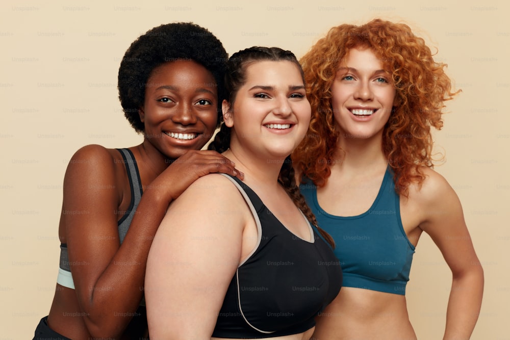 Different Women. Group Of Diversity Models Portrait. Smiling International Female In Fitness Clothes Posing On Beige Background. Body Positive As Lifestyle.