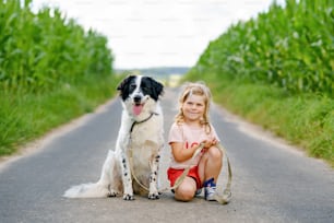 Cute little preschool girl going for a walk with family dog in nature. Happy smiling child having fun with dog, run and hugging. Happy family outdoors. Friendship and love between animal and kids.