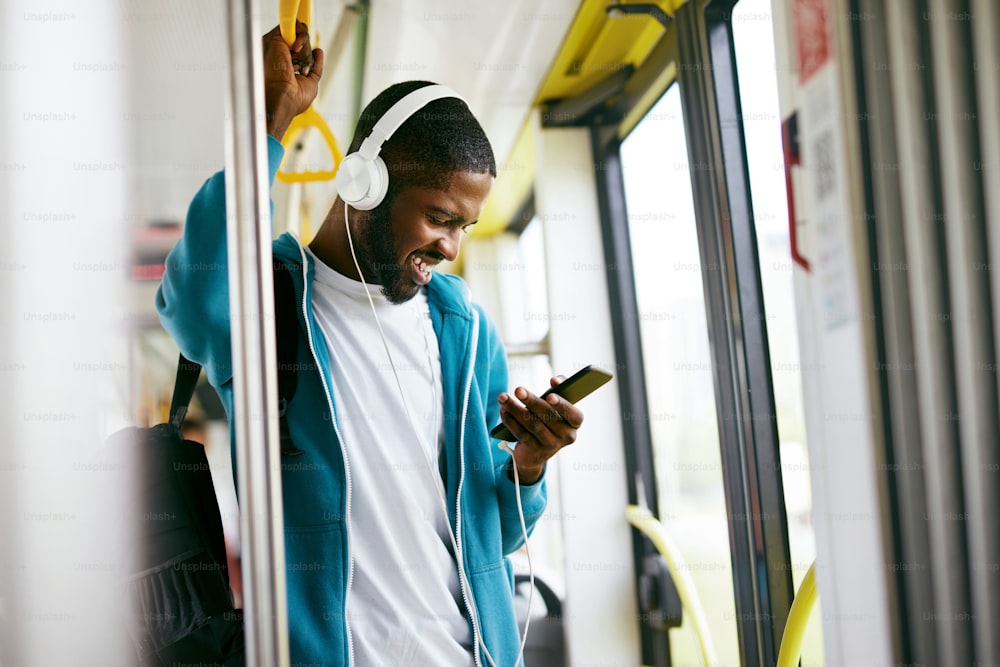 Homme utilisant le téléphone, écoutant de la musique voyageant dans le train. Étudiant noir avec des écouteurs dans les transports en commun. Haute résolution