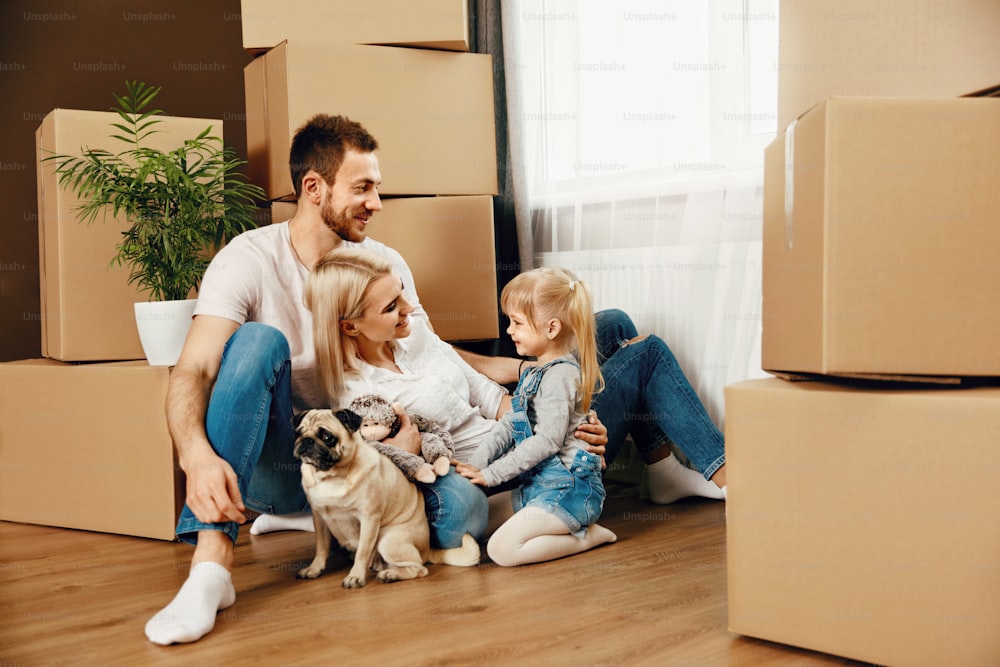 Famiglia felice con bambino e cane seduti vicino a scatole di cartone in un nuovo appartamento accogliente. Alta risoluzione.