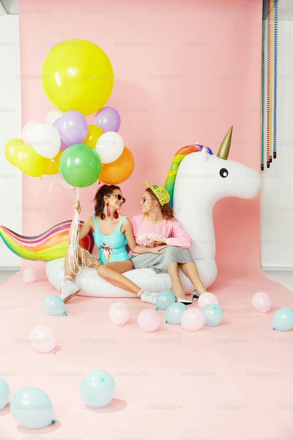 Diversión de verano. Mujeres felices amigas en ropa de moda con globos. Hermosas chicas sonrientes con ropa colorida de moda sentadas en un flotador inflable de unicornio sobre fondo rosa. Alta resolución