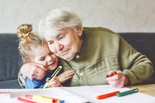 Menina bonita e bisavó desenhando juntos fotos com canetas de feltro em casa. Criança bonito e mulher sênior se divertindo juntos. Família feliz dentro de casa.