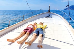 Two little kid boys, best friends enjoying sailing boat trip. Family vacations on ocean or sea on sunny day. Children smiling. Brothers, schoolchilden, siblings having fun on yacht