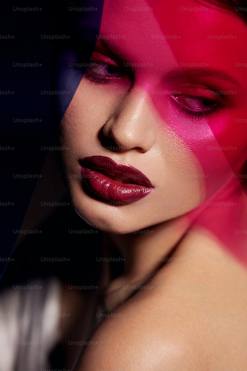 Beauty-Gesichts-Make-up. Modeporträt eines Mädchenmodells mit Lippenstift unter Farbe. Nahaufnahme eines glamourösen Mädchens mit sexy dunkelroten Lippen, Make-up und strahlender Haut unter rosa und lila Farben. Hochwertige