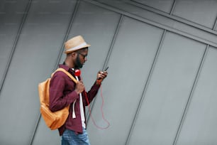 Bello uomo nero in vestiti di moda con telefono sulla strada. Elegante uomo africano con cuffie e telefono in città. Alta risoluzione