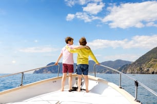 Two little kid boys, best friends enjoying sailing boat trip. Family vacations on ocean or sea on sunny day. Children smiling. Brothers, schoolchilden, siblings, best friends having fun on yacht