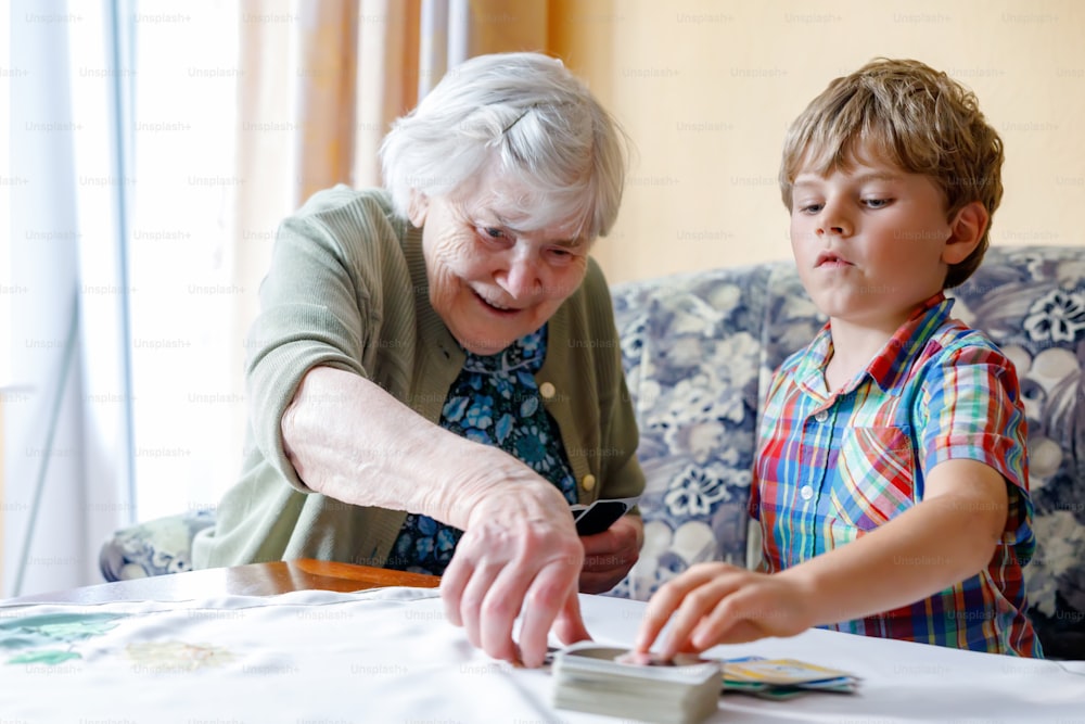 활동적인 작은 미취학 아동 소년과 할머니가 집에서 함께 카드 게임을 하고 있다. 어린 아이와 은퇴한 여자가 즐거운 시간을 보내고 있다. 행복한 가족: 손자와 노인