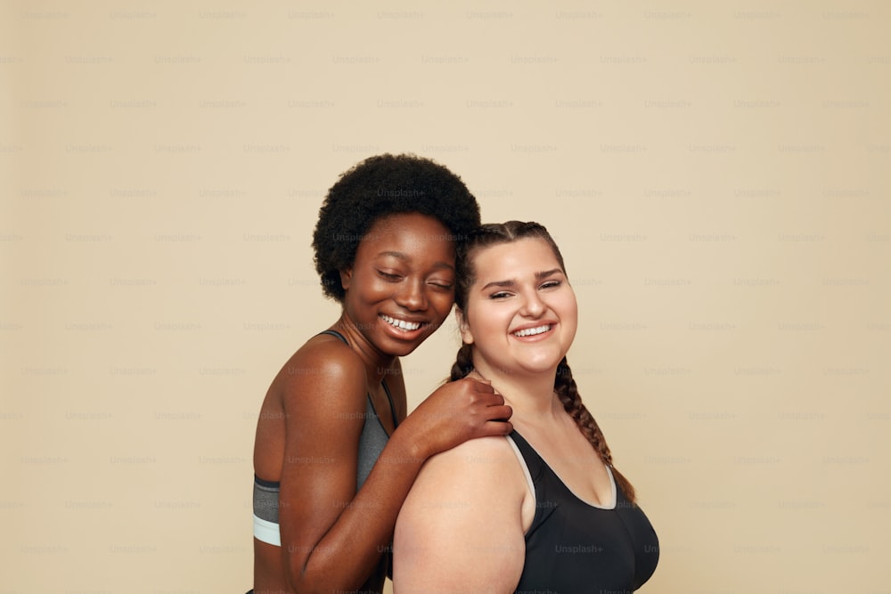 Fitness. Caucasian And African Women Portrait. Different Race Models In Fitness Clothes Posing On Beige Background. Body Positive As Lifestyle.