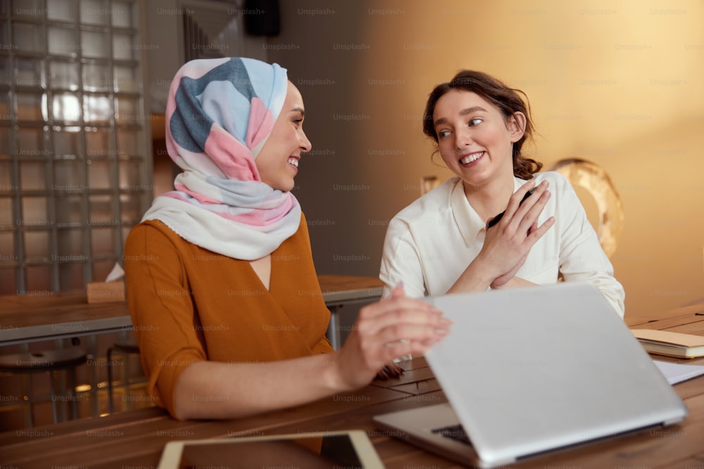 Business. Women Meeting In Cafe. Diversity Ethnic Colleagues Finishing Work On Laptop. Thankful Brunette Looking At Girl In Hijab.