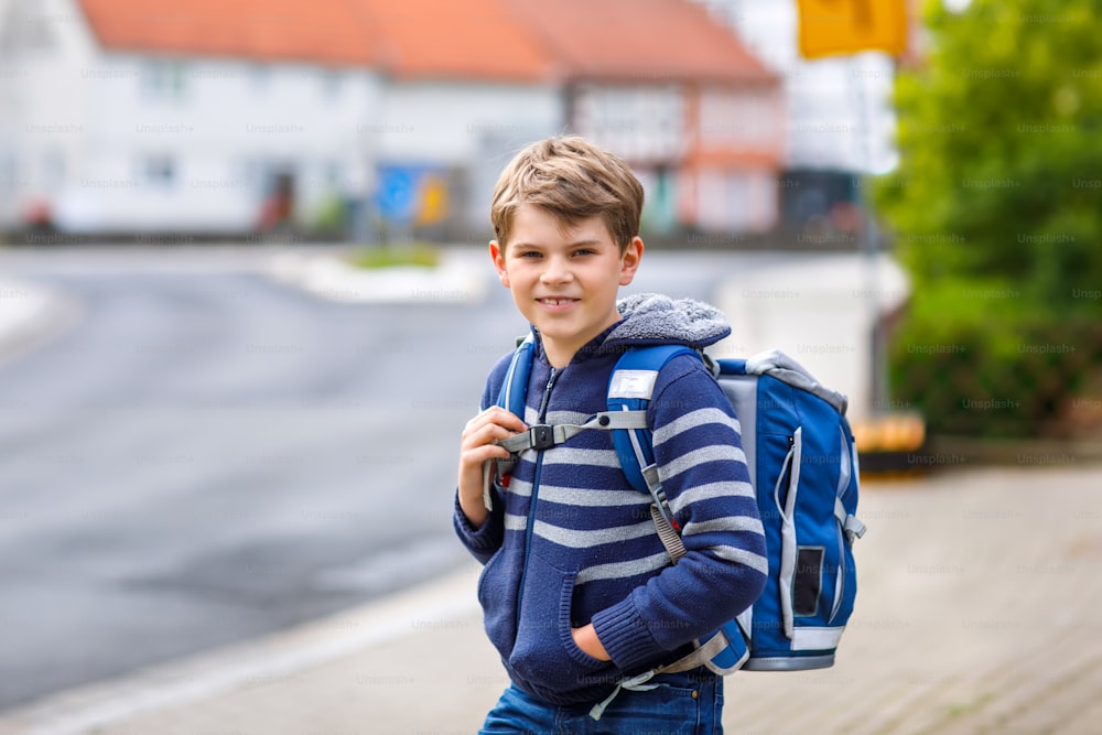 Happy little kid boy with backpack or satchel. Schoolkid on way to elementary school. Healthy adorable child outdoors. Back to school after quarantine time from corona and covid 19 pandemic disease.