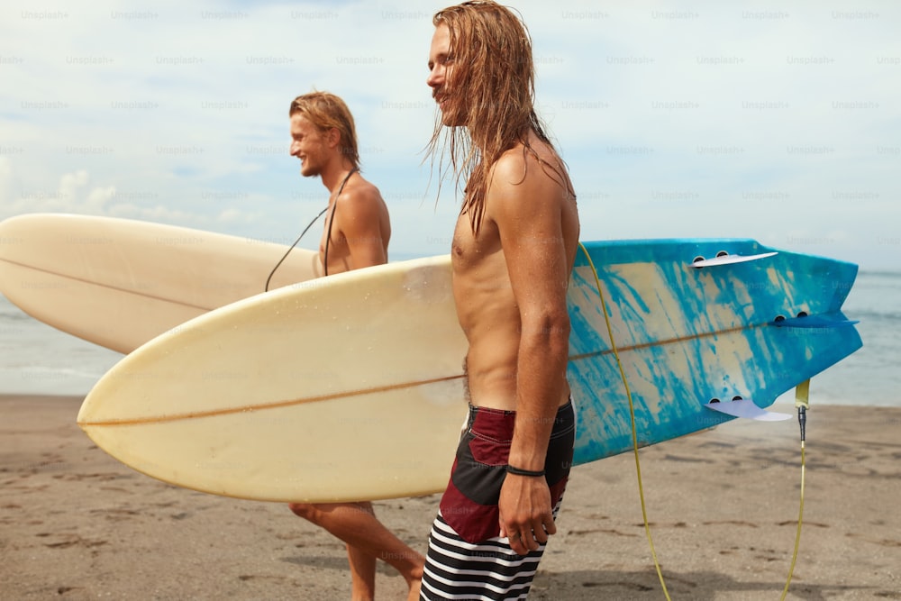 Surfe. Surfistas bonitos com pranchas de surf. Rapazes caminhando na praia do oceano. Estilo de vida ativo, esporte aquático no fundo do mar bonito.