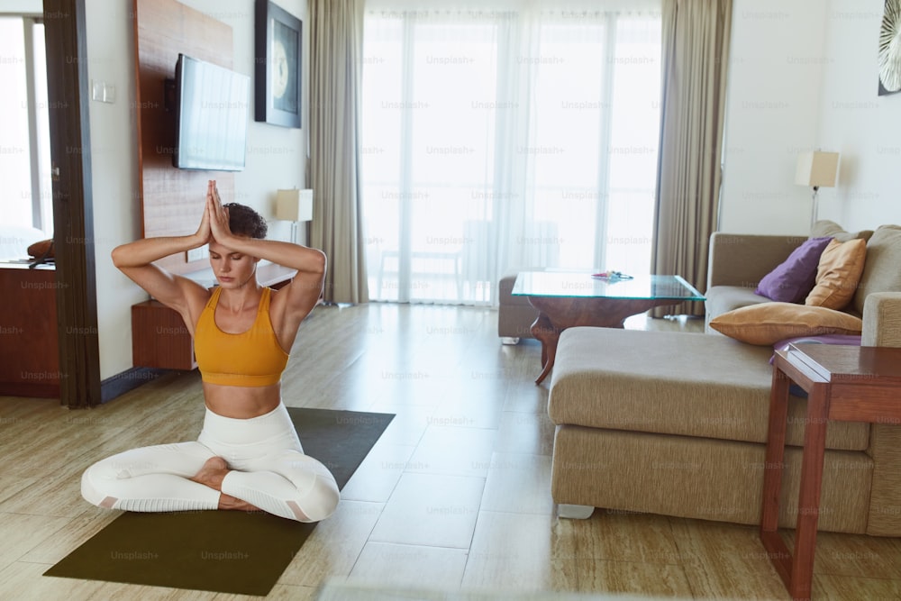 Meditation. Woman In Easy Pose Practicing Yoga At Home. Young Female Sitting On Floor And Keeping Hands Above Head. Sport Routine For Staying Calm And Healthy During Quarantine.