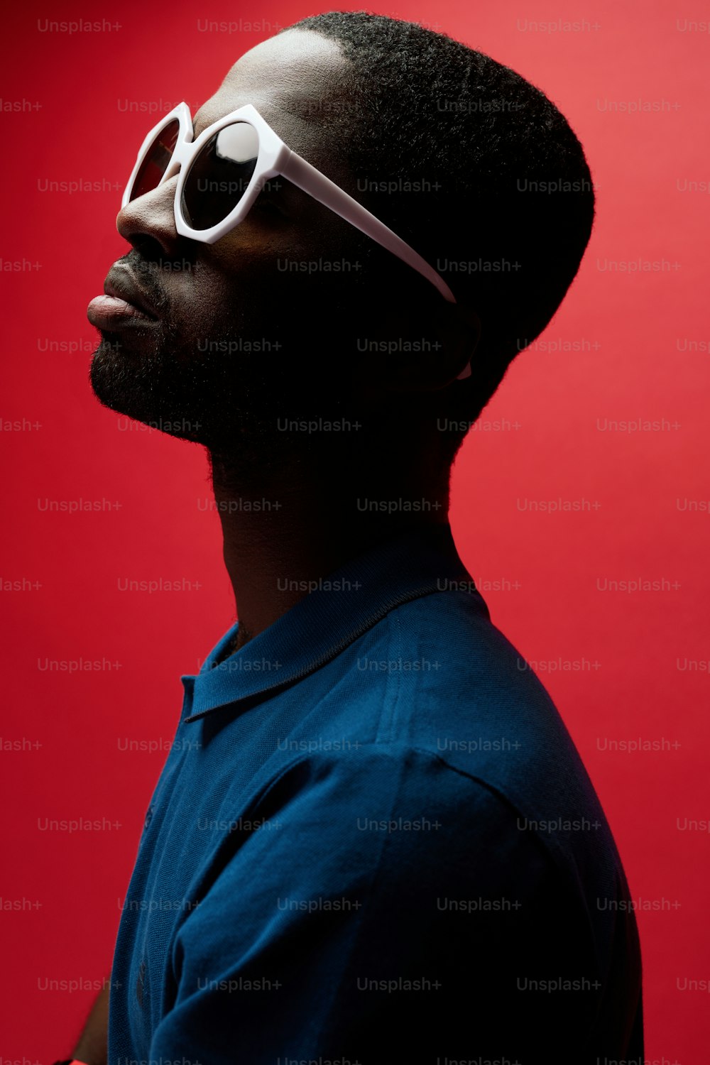 Portrait de mode d’homme noir portant des lunettes de soleil sur fond rouge. Beau mannequin masculin afro-américain avec une tenue élégante posant au studio