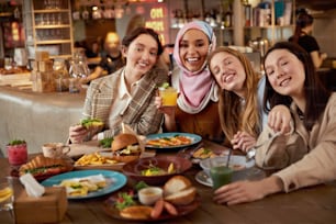 Almuerzo. Grupo de mujeres en el retrato del café. Sonrientes chicas multiculturales con cócteles. Reunión de amigos en restaurante como parte del estilo de vida.