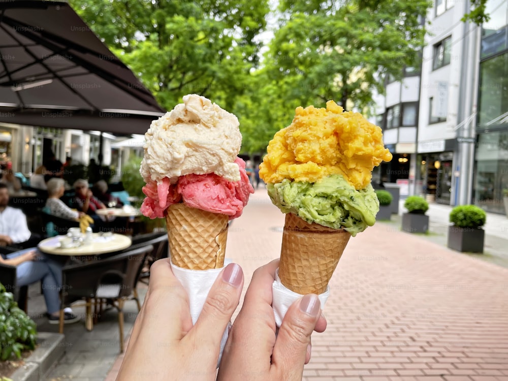 Young woman hands holding ice cream cones on summer day in the city. Tasty colorful fruit and berry ice cream.