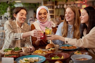 Almoço. Moças no Retrato do Café. Grupo de meninas multiétnicas sorridentes torcendo com coquetéis. Encontro de amigos no restaurante como parte do estilo de vida.