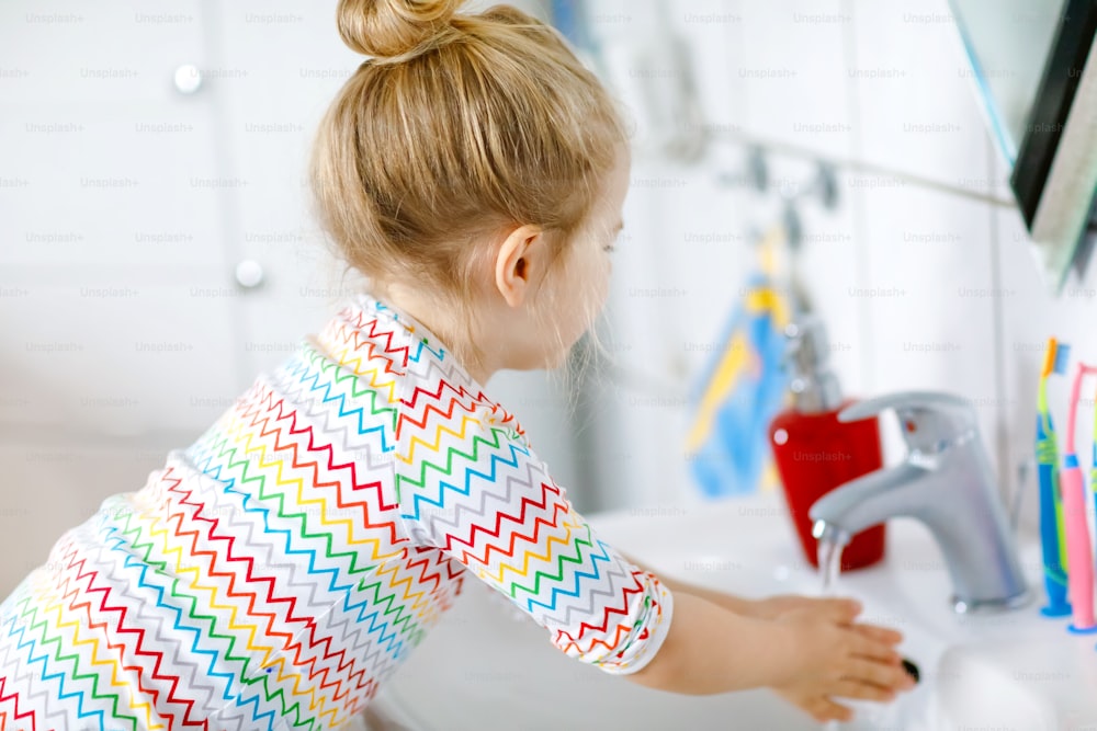 귀여운 어린 소녀가 욕실에서 비누와 물로 손을 씻고 있다. 신체 부위를 청소하는 것을 배우는 사랑스러운 아이. 바이러스 제거 중 위생 일상적인 조치. 집이나 보육원에 있는 아이