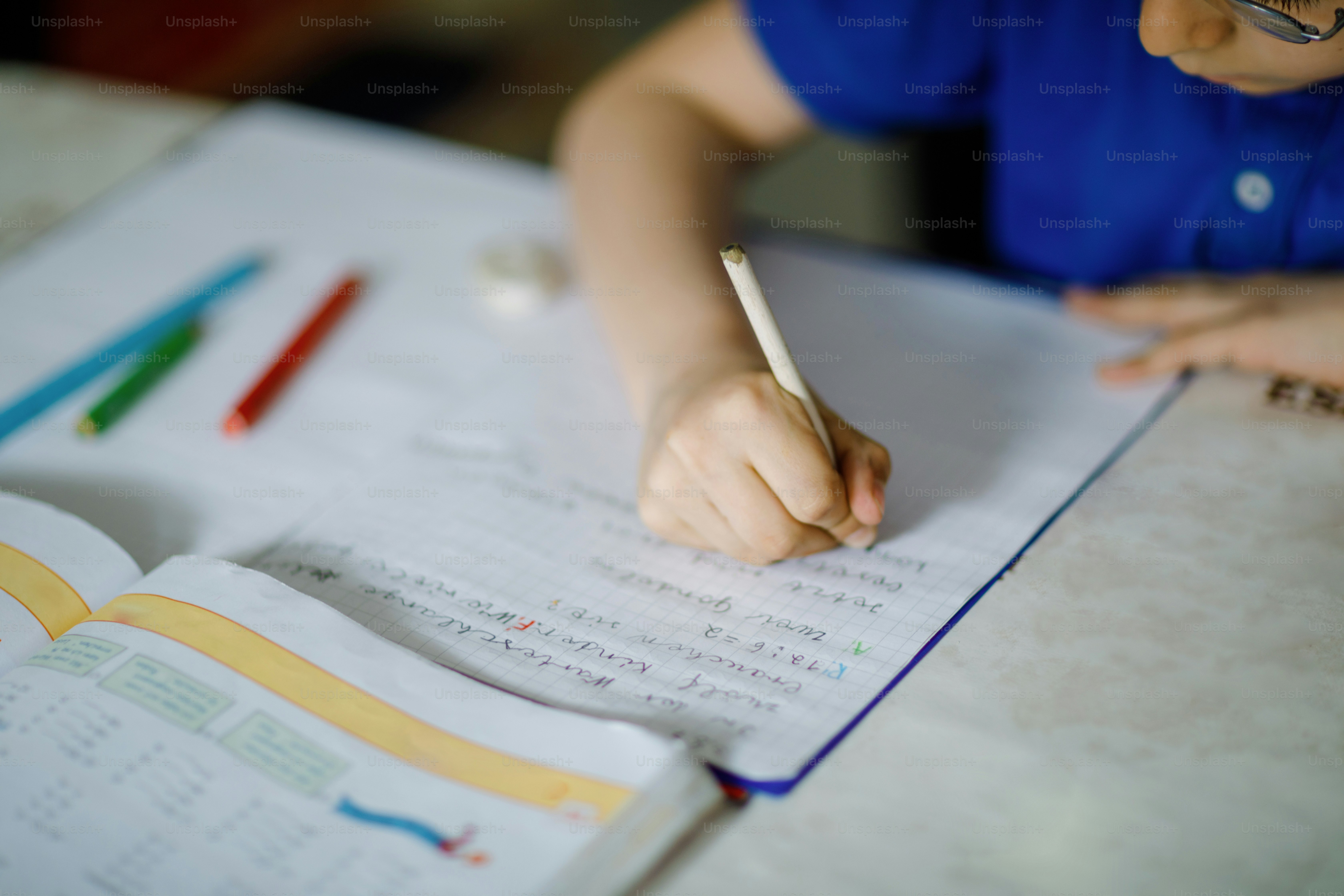 Close-up of little kid boy with glasses at home making homework, writing letters with colorful pens. Little child doing exercise, indoors. Elementary school and education, home schooling concept