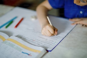 Close-up of little kid boy with glasses at home making homework, writing letters with colorful pens. Little child doing exercise, indoors. Elementary school and education, home schooling concept