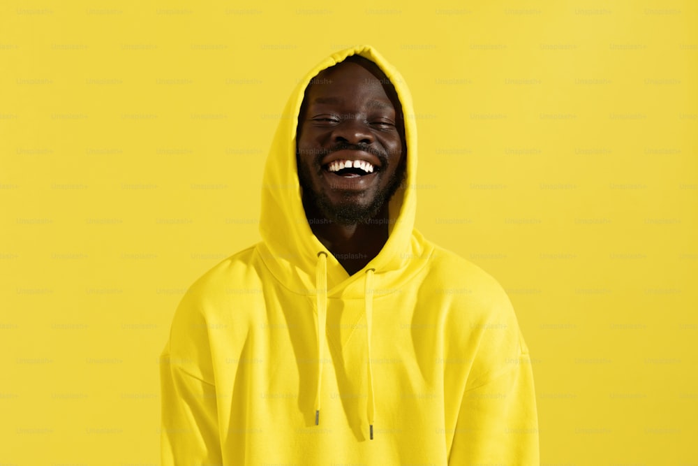 Portrait of happy black man in yellow hoodie on color background. Cheerful smiling african american male model with white smile in stylish sweatshirt with hood on head in studio