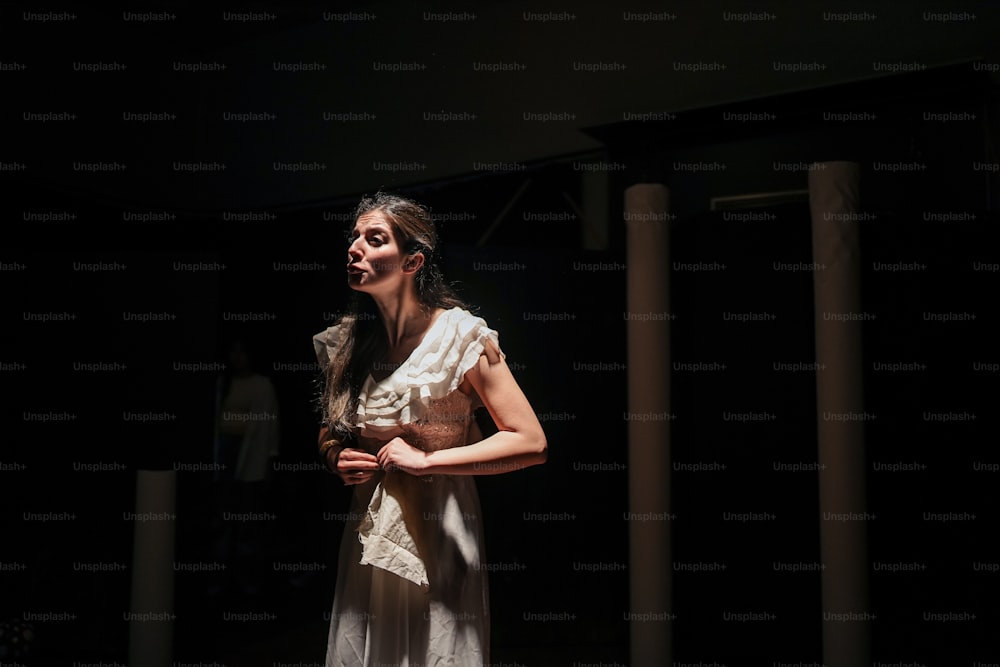 Una mujer con un vestido blanco parada en una habitación oscura