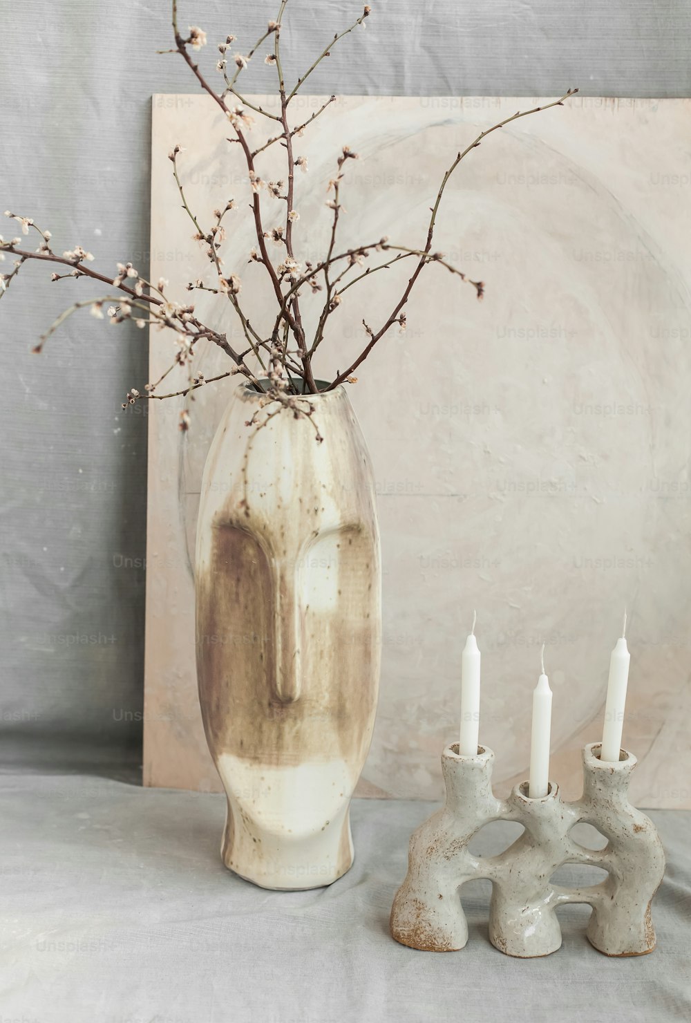 a vase with a branch in it next to three candles