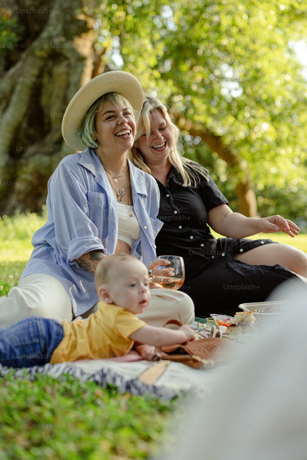 duas mulheres e um bebê sentados em um cobertor em um parque