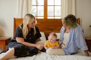 two women and a baby sitting on a bed