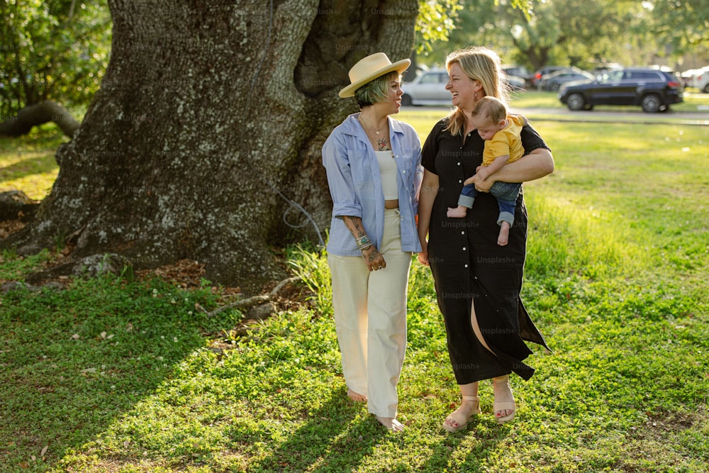 two women and a baby are standing under a tree