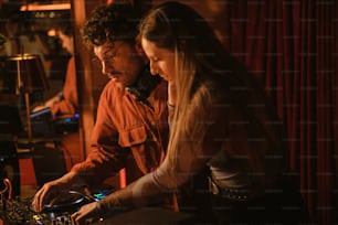 Um homem e uma mulher olhando para o equipamento de um DJ