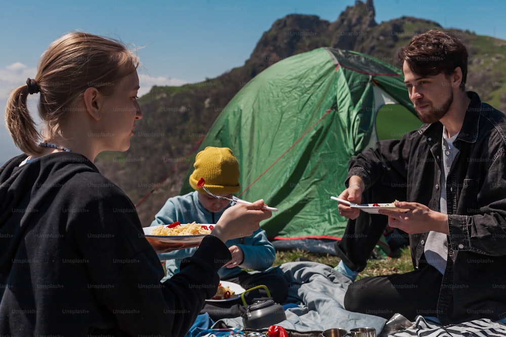 a man and a woman eating food at a campsite
