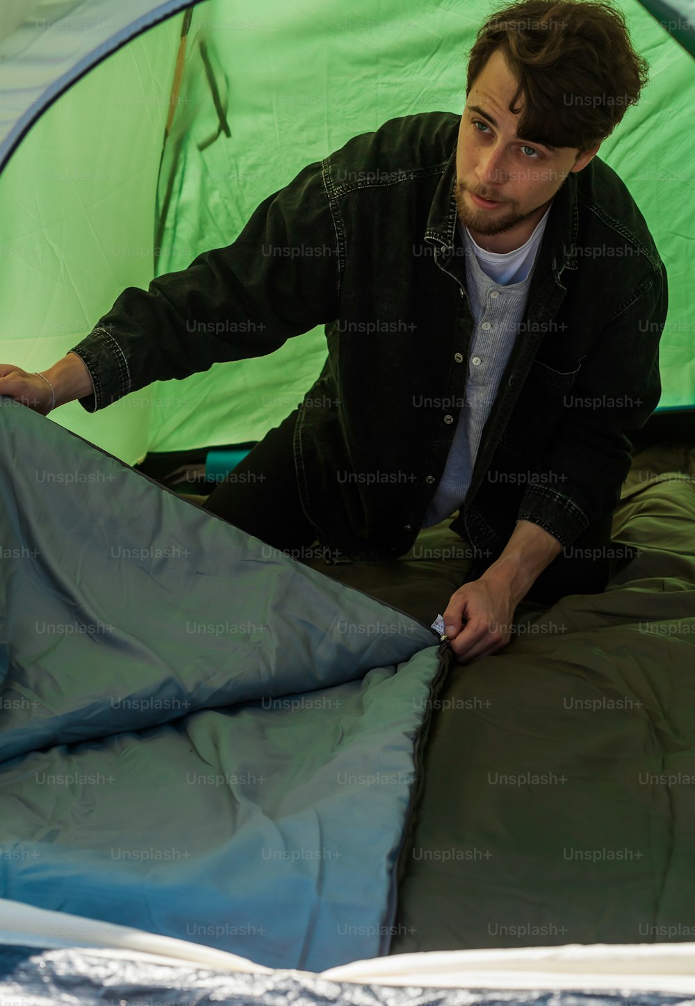 Un hombre sentado dentro de una tienda de campaña con un saco de dormir