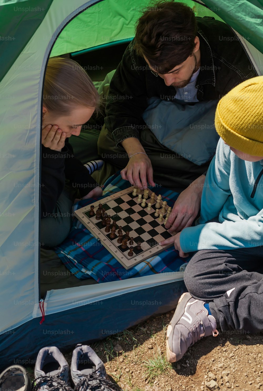 Tres personas jugando una partida de ajedrez en una tienda de campaña