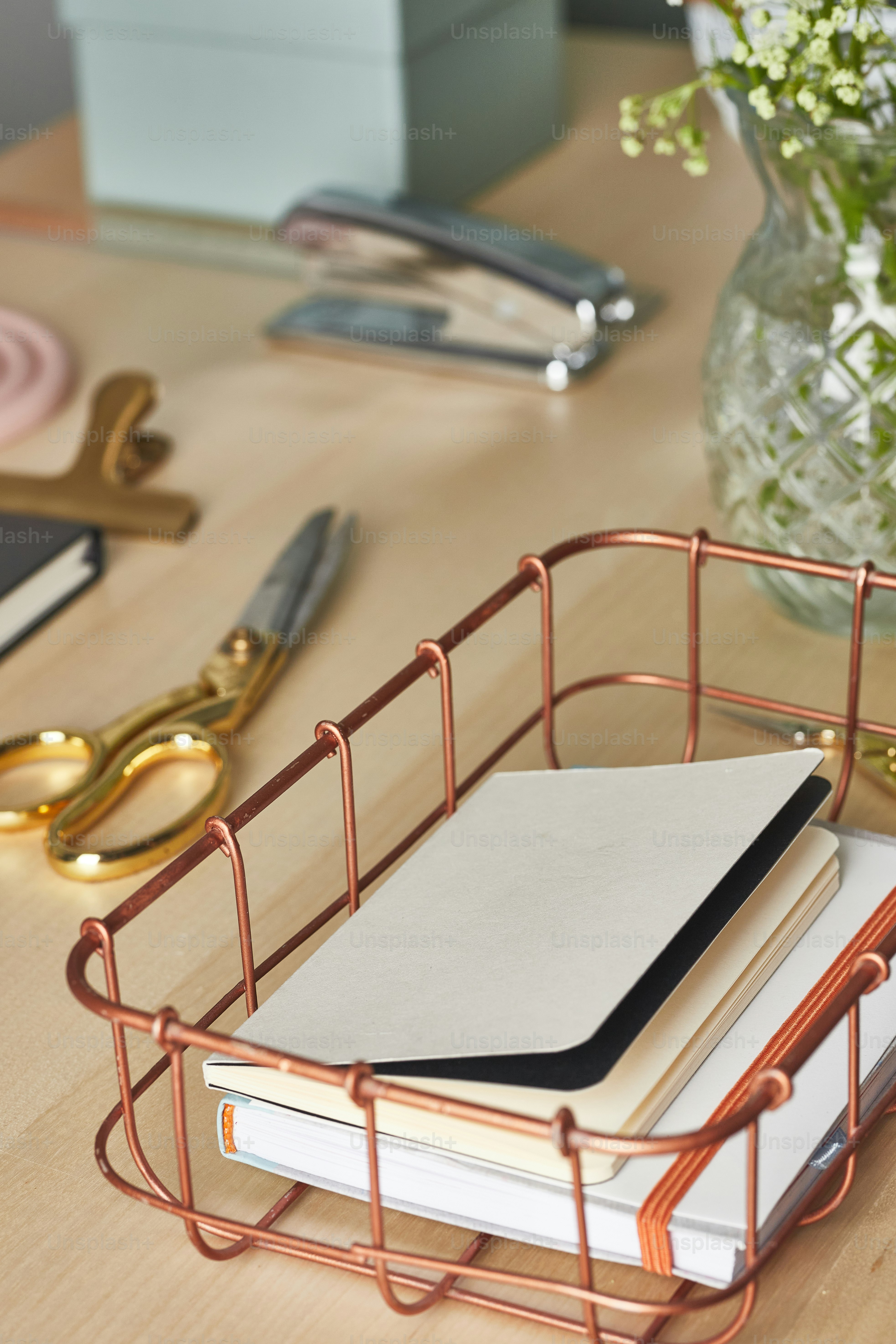 a desk with a pen, notebook, scissors, and a vase of flowers