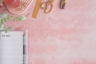 a pink desk with a notepad, pen, scissors and a plant