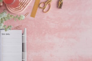 un bureau rose avec un bloc-notes, un stylo, des ciseaux et une plante