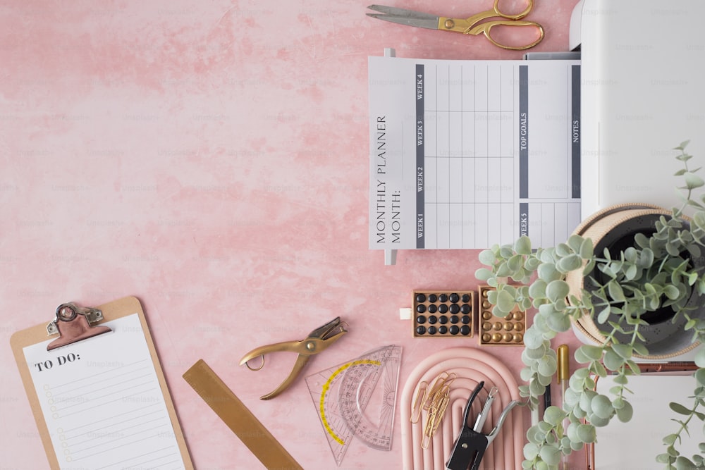 Un escritorio rosa con un portapapeles y una planta