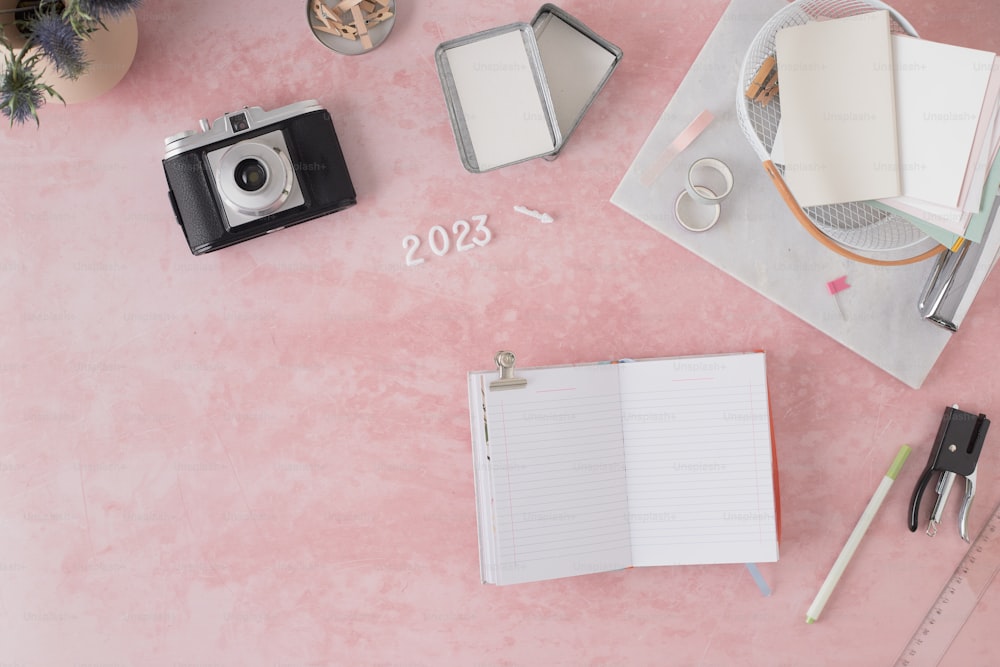 une table rose avec un appareil photo, un cahier et un stylo