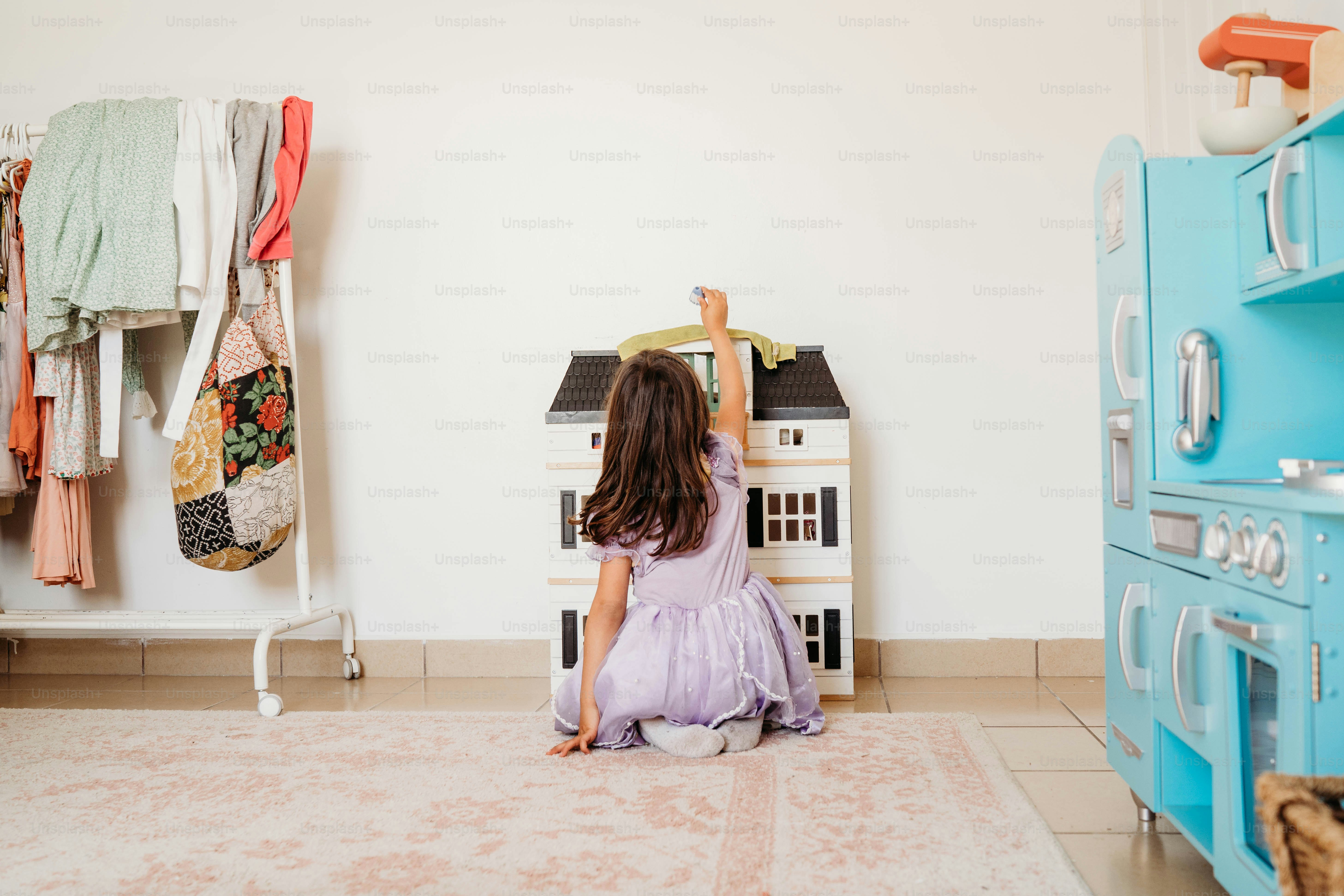 Une petite fille assise par terre devant une maison de poupée
